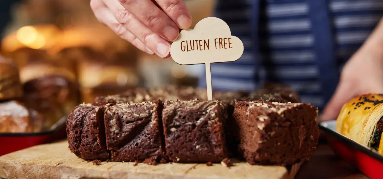 Baker placing a gluten free sign into sliced chocolate brownies on a wooden board.