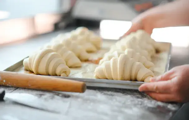 Baker holding a tray of unbaked croissant dough ready for the oven.