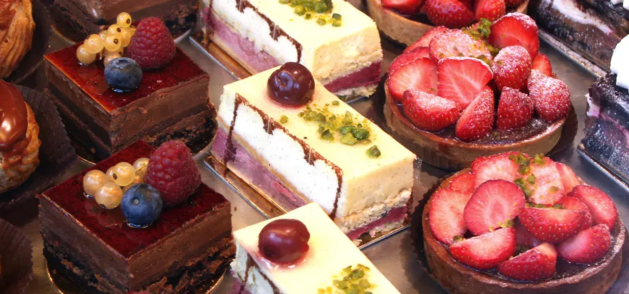 Assorted bakery desserts including chocolate cakes, vanilla cream slices, and strawberry tarts on display.