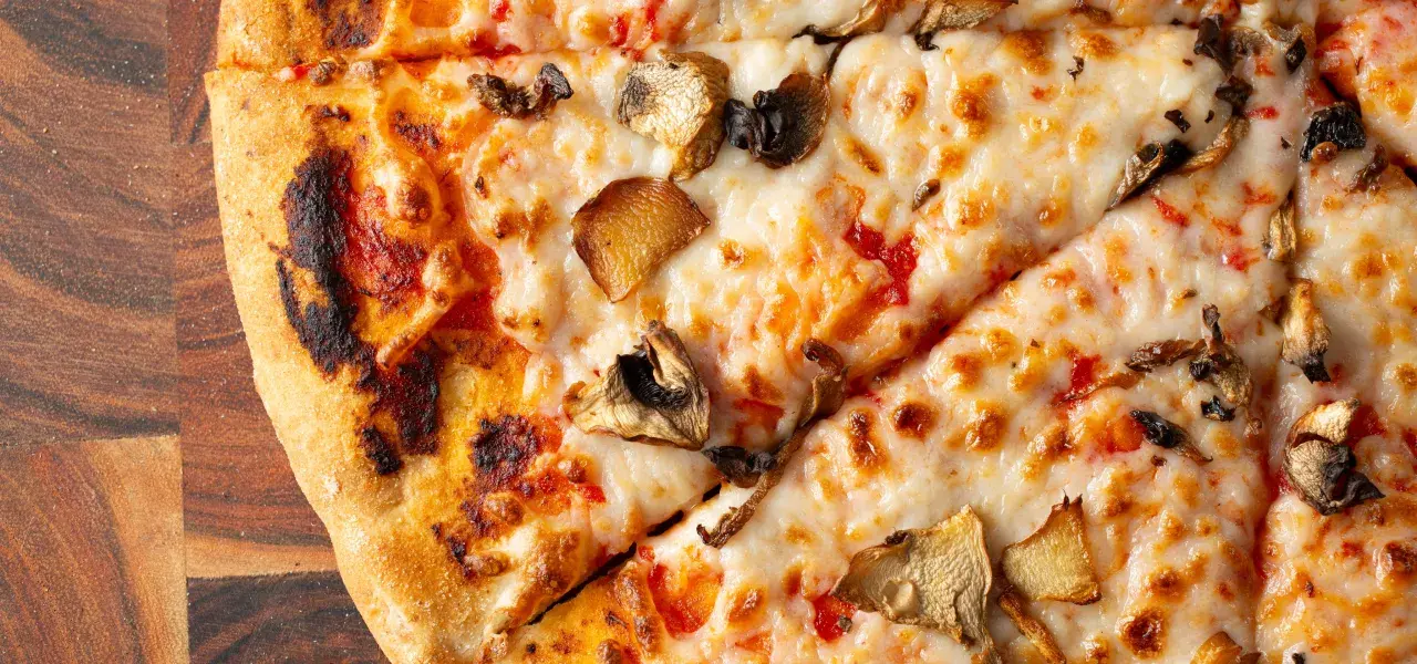 Sliced mushroom pizza with melted cheese on a wooden cutting board.