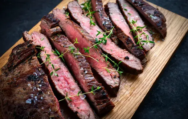 Sliced medium rare steak topped with fresh thyme on a wooden cutting board.