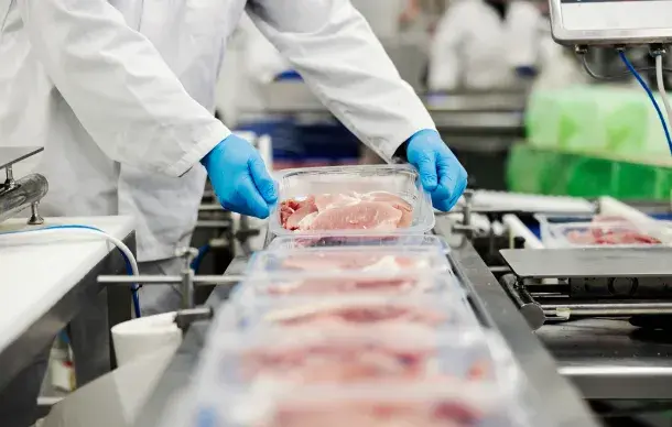 Worker packaging fresh meat on a processing line.