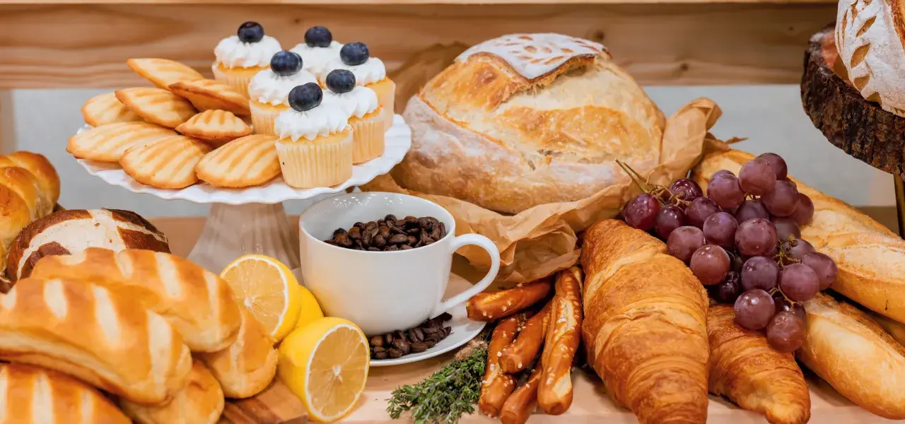 Bakery spread with fresh bread, croissants, madeleines, cupcakes, pretzels, and a cup of coffee beans.