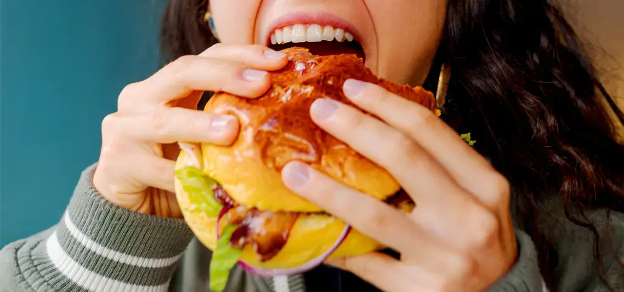Woman taking a bite of a burger with lettuce and onion on a brioche bun.
